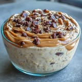 A jar of overnight oats layered with creamy peanut butter and mini chocolate chips, topped with banana slices for a wholesome breakfast.