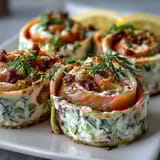 Smoked salmon and cucumber cream cheese pinwheels arranged on a white platter with fresh dill garnish.