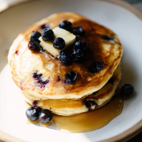 Warm stack of homemade blueberry pancakes, piled high, ready to be drizzled with sweet maple syrup.