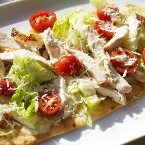 Warm Chicken Caesar Flatbread served with crisp lettuce, cherry tomatoes, and shaved parmesan on an appetizer platter.