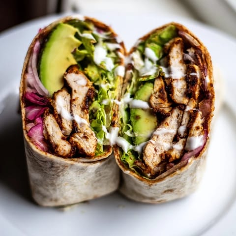Smoky Chipotle Chicken Wrap drizzled with creamy Greek yogurt sauce and topped with fresh diced tomatoes and thin red onion slices on a rustic wooden board.