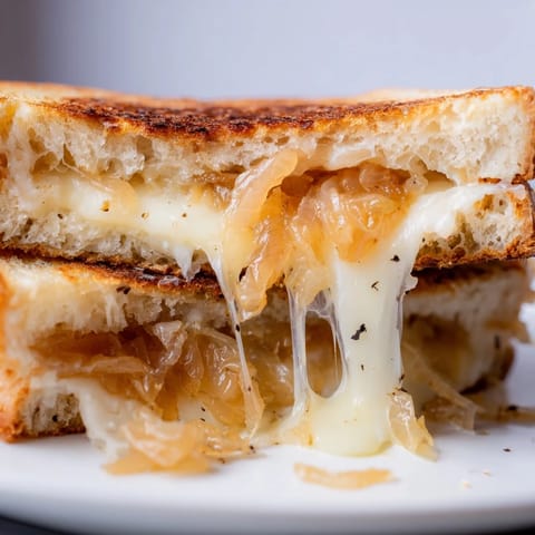 Golden, buttery sourdough sandwiches stuffed with sweet caramelized onions and melted sharp white cheddar, served hot beside a steaming bowl of tomato soup.  