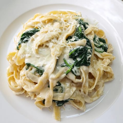 Steam rises from a serving of Creamy Garlic Spinach Pasta, garnished with fresh parsley and a generous sprinkle of Parmesan cheese.