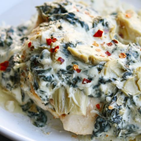 Tender baked chicken breasts smothered in creamy spinach and artichoke yogurt topping, served as a main dish.  