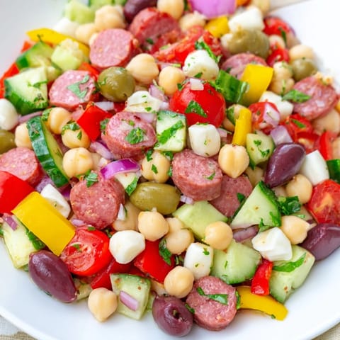 Close-up of Crunchy Antipasto Chopped Salad featuring diced peppers, cucumbers, olives, and fresh herbs on a rustic plate.